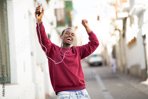 Excited young african man enjoying listening to music and dancing in the city © mimagephotos