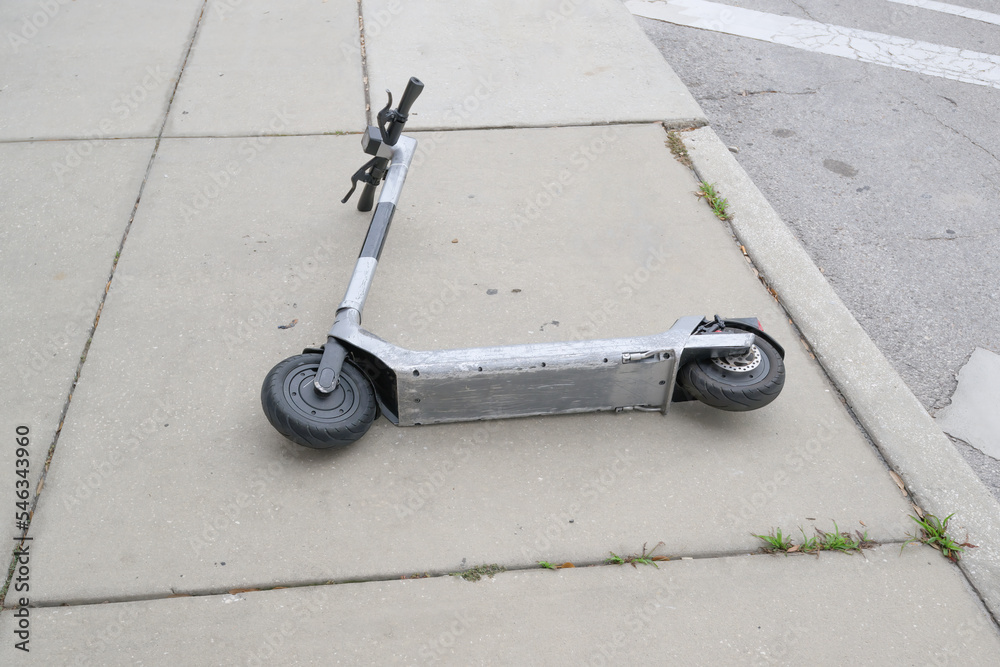 scraped-up silver electric scooter lying down on the sidewalk
