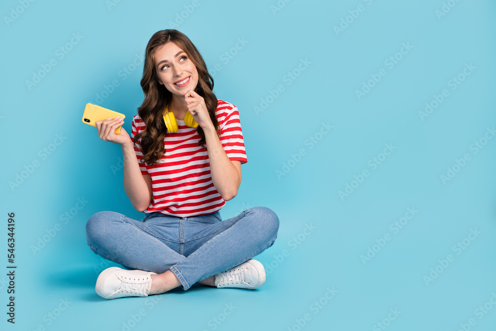Full length photo of funky dreamy girl dressed red t-shirt arm chin chatting modern gadget empty space isolated blue color background Full length photo of funky dreamy girl dressed red t-shirt arm chin chatting modern gadget empty space isolated blue color background