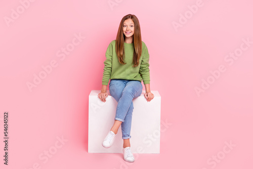 Full length photo of pretty sweet school girl dressed green sweatshirt sitting white cube chair isolated pink color background