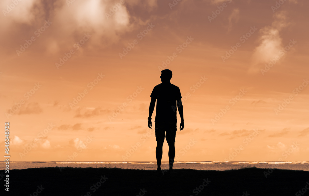 Silhouette of young man looking out to the ocean view. 