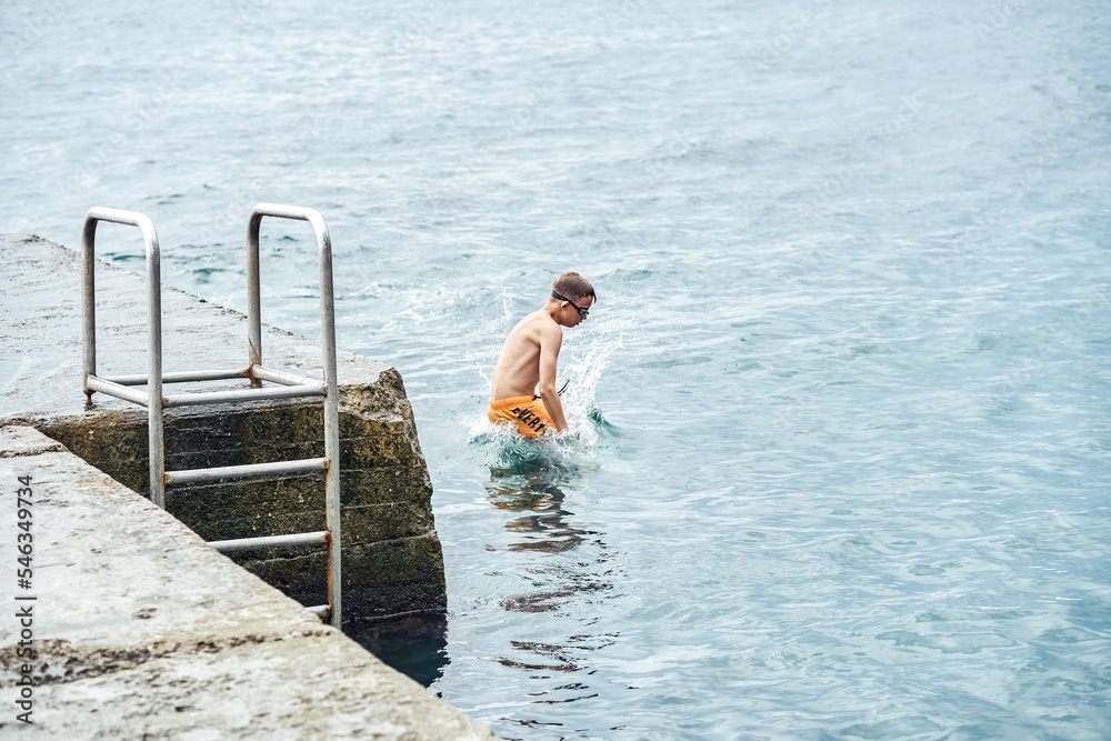 Moments of schoolboy jumping from stone pier with ladder into sea doing tricks in combined image sequence Moments of schoolboy jumping from stone pier with ladder into sea doing tricks in combined image sequence