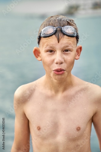 Funny and surprised teenager in swimming goggles all wet stands posing against sea pebble beach