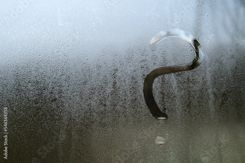 A question mark is drawn on glass with condensation, the effect of fogged windows and glass.