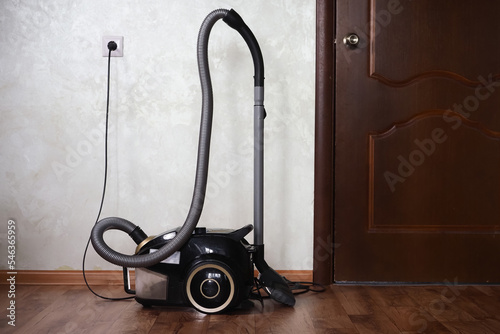  black vacuum cleaner plugged into a socket stands in a room on the floor