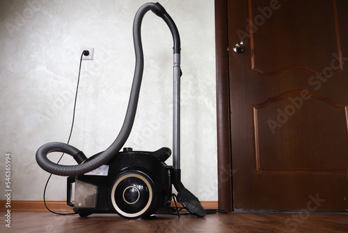  black vacuum cleaner plugged into a socket stands in a room on the floor