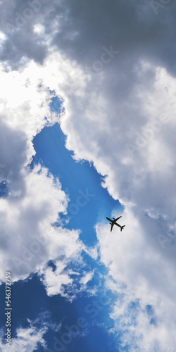 The passenger airplane is flying far away in the blue sky. Dramatic clouds with the sun shining through them. Aircraft in the air. Vertical illustration. Passenger air transportation