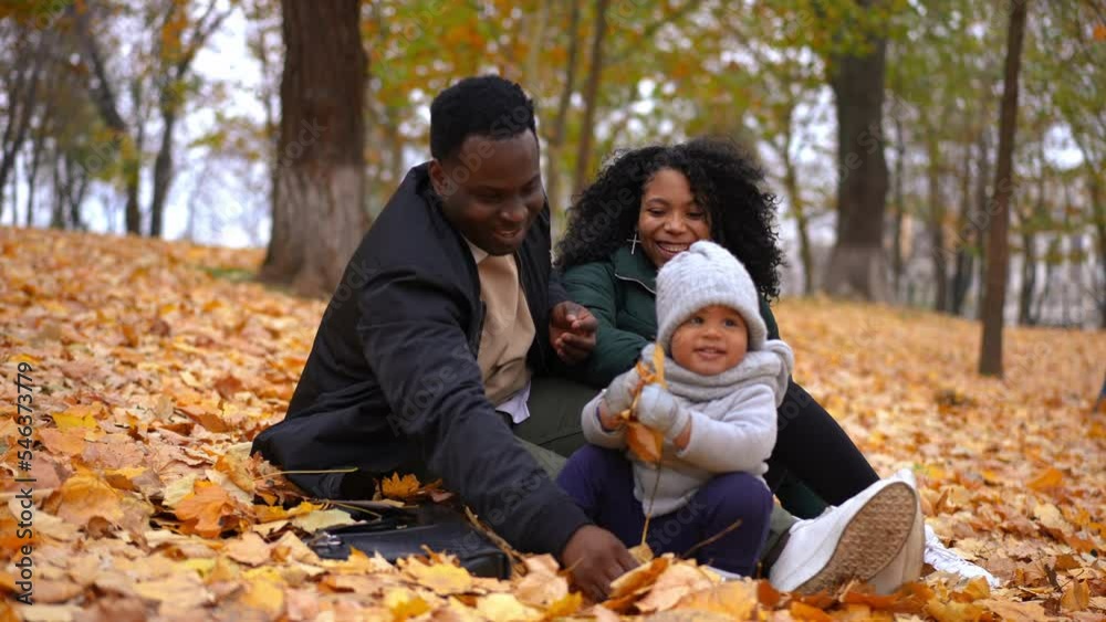 Cheerful young father and mother tossing yellow leaves having fun with toddler son in autumn park. Happy carefree African American man and woman enjoying leisure with boy outdoors