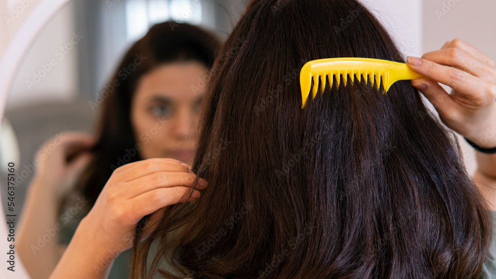 Fototapeta premium Girl touching her hair while looking in the mirror. Hair care