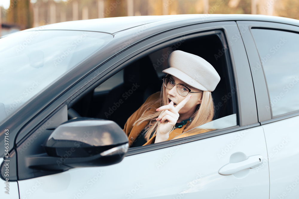 Naklejka premium excited middle aged flirtatious woman holding steering wheel gesturing and driving car