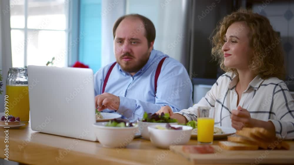 Young couple have breakfast and use laptop in kitchen at home. Realtime Young couple have breakfast and use laptop in kitchen at home. Realtime