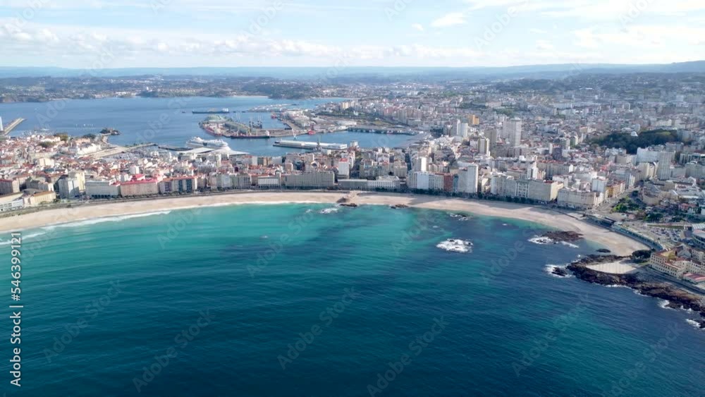 Drone point of view of Galician city A Coruna. View of famous beach Orzan. In background the city center and the harbour area. Drone backward Travel destination in Northwest of Spain 