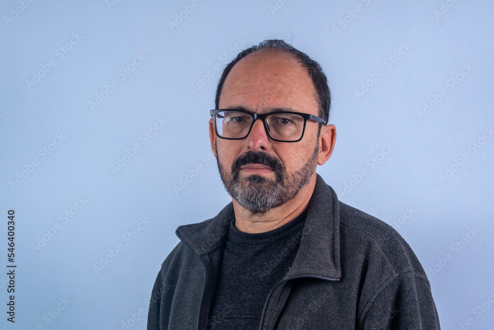 Portrait of 60 years old bearded man on blue background with hat and glasses