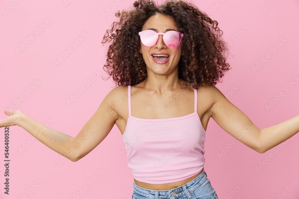 Happy woman afro curls hair dancing on a pink background in summer pink t-shirt jeans and glasses, summer vibe, copy space Happy woman afro curls hair dancing on a pink background in summer pink t-shirt jeans and glasses, summer vibe, copy space