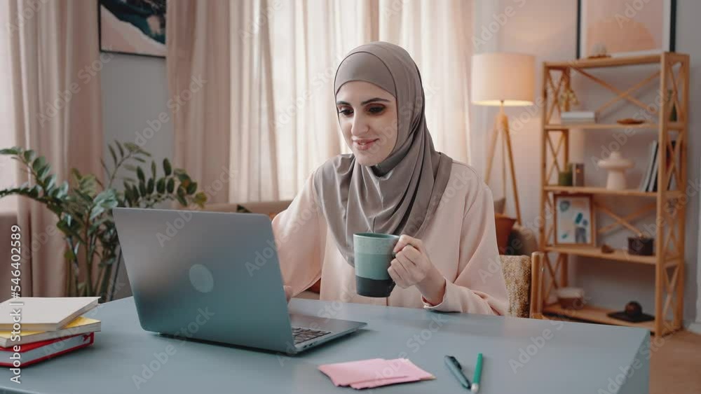 Young Arabian woman works on laptop and drinks hot beverage Young Arabian woman works on laptop and drinks hot beverage