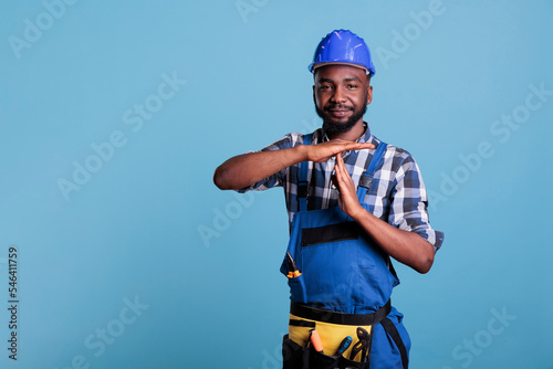 Construction worker making the pause gesture on camera, showing the T-shaped stop sign with arms in the studio. African american builder requesting time out for a short break, wearing hard hat and