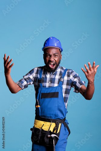 Outraged employee handyman in protective helmet outstretched hands scream isolated on blue background. Instruments accessories for construction and renovation, studio shot.
