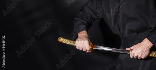 The samurai holding a Japanese katana sword, banner. Photo of a warrior dressed in black clothes in low key with copy space for text photo