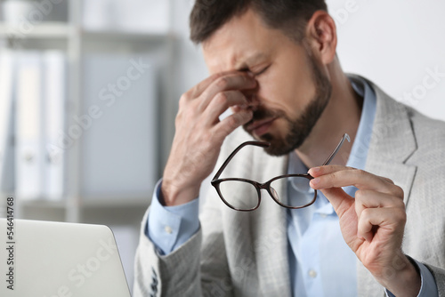 Man suffering from eyestrain in office, focus on hand with glasses