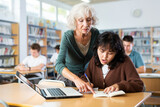 Mature woman teacher working with schoolchildren in the library cheks the assignment from a asian fifteen-old-year schoolgirl