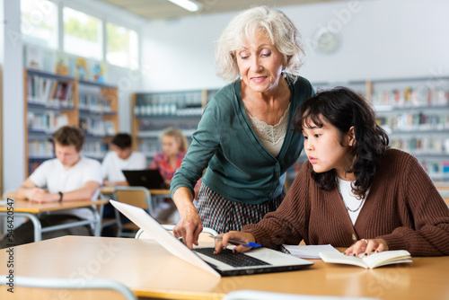Elderly female teacher helps schoolgirl solve the equation in the school library