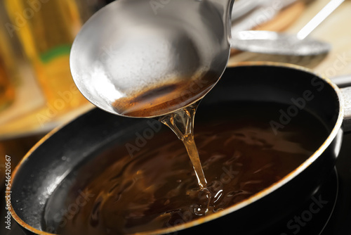 Pouring used cooking oil with ladle onto frying pan on stove  closeup