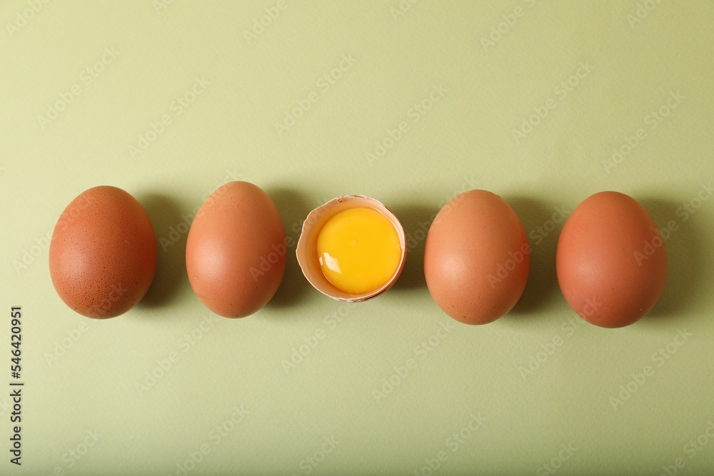 Cracked and whole chicken eggs on olive background, flat lay Cracked and whole chicken eggs on olive background, flat lay