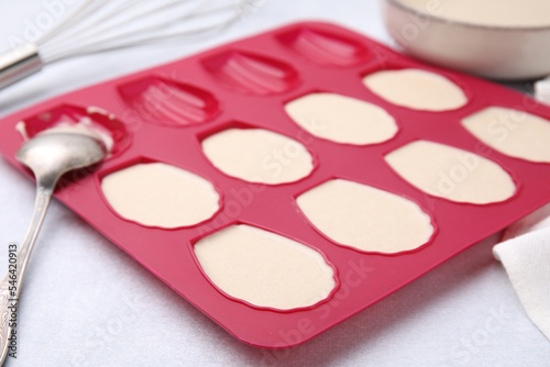 Baking mold for madeleine cookies with batter on white table  closeup