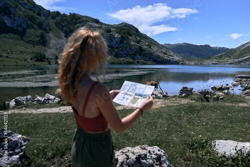 blonde caucasian girl looking at the map near the calm lake in nature, covadonga asturias, spain