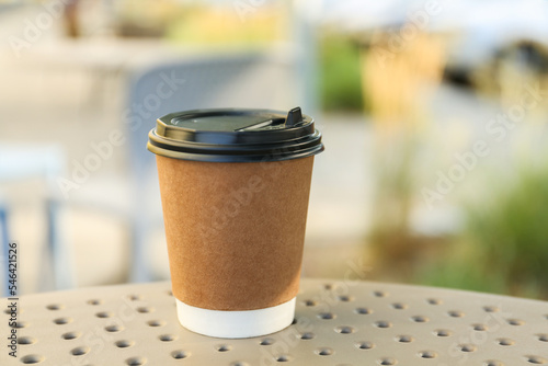 Paper cup with hot coffee on table outdoors, closeup. Takeaway drink