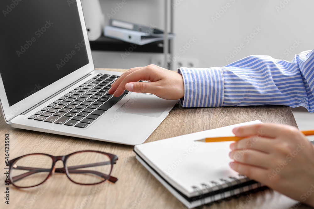 Woman with notebook working on laptop at wooden table in office, closeup Woman with notebook working on laptop at wooden table in office, closeup