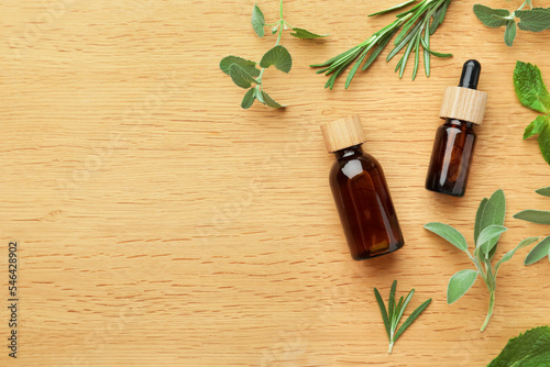 Bottles of essential oils and fresh herbs on wooden table, flat lay. Space for text