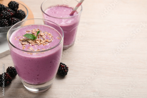 Delicious blackberry smoothie with oatmeal in glass on white wooden table, space for text