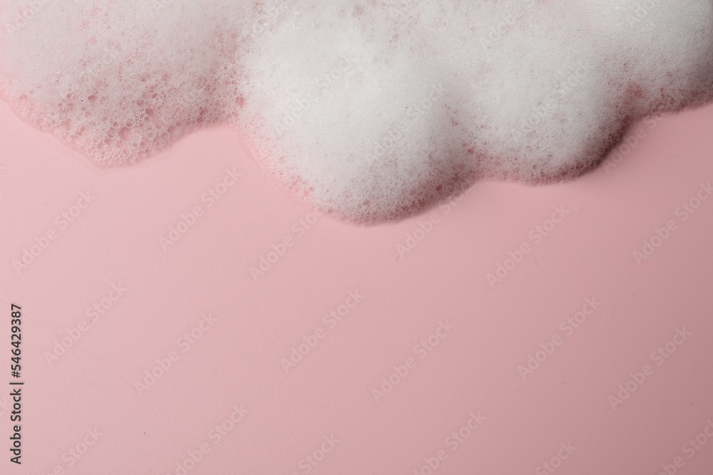 Fluffy soap foam on pink background, above view. Space for text
