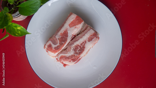 Shortplate sliced fresh beef meat isolated in white plate and red table photo