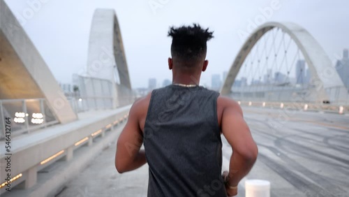 African American man working out by jogging across the 6th Street Bridge in Los Angeles at dawn on an overcast morning. Downtown LA can be seen in the background. Jogger has a deformed left hand. photo