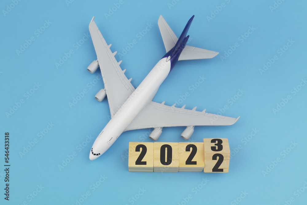 Airplane and wooden cubes with 2022 and 2023 on blue background. 