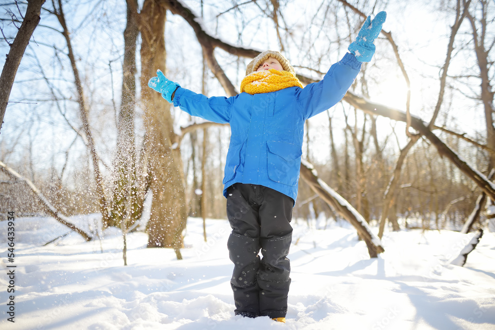 Little boy throwing fresh snow from his hands. Child enjoy walking in the park on snowy day. Baby having fun during snowfall. Outdoor winter activities for kids.
