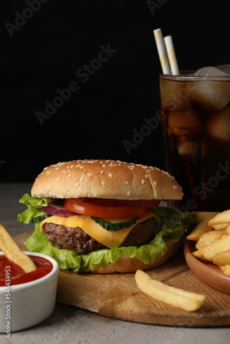 Delicious burger, soda drink and french fries served on grey table, closeup