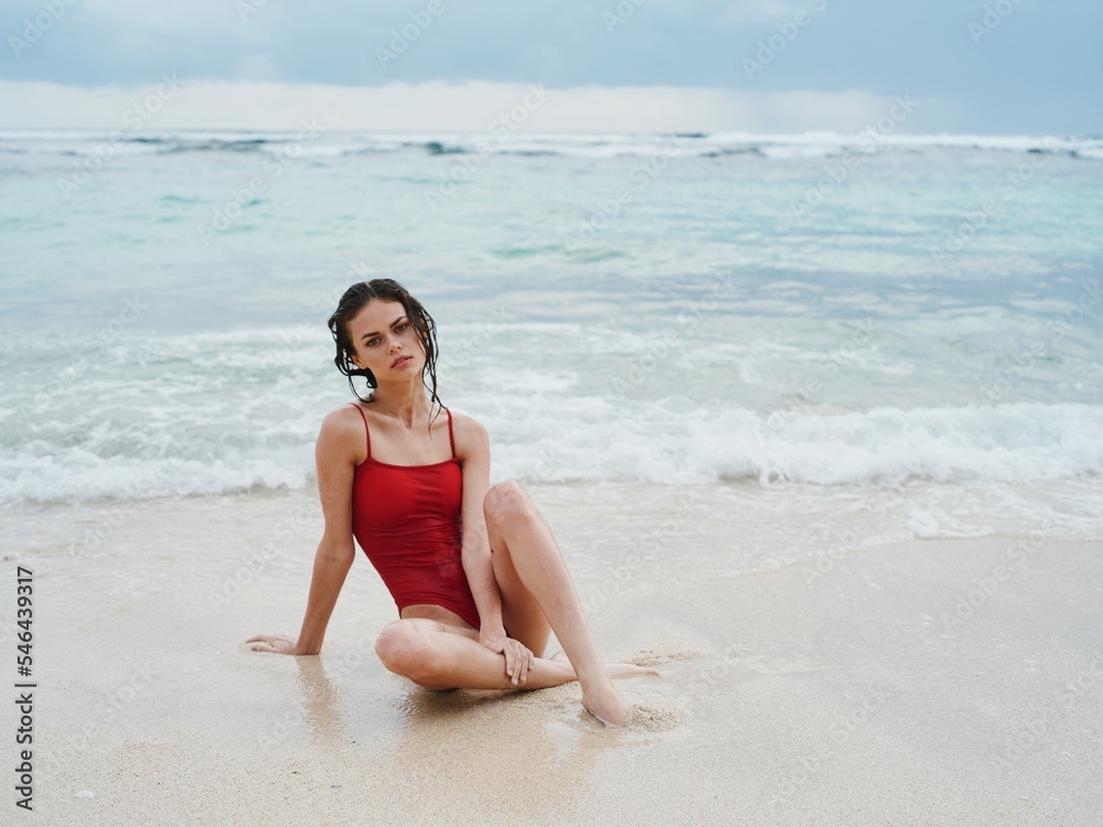Woman with wet hair after swimming in the ocean in a red swimsuit sits on the beach in Bali and looks into the camera, a trip to Indonesia Woman with wet hair after swimming in the ocean in a red swimsuit sits on the beach in Bali and looks into the camera, a trip to Indonesia