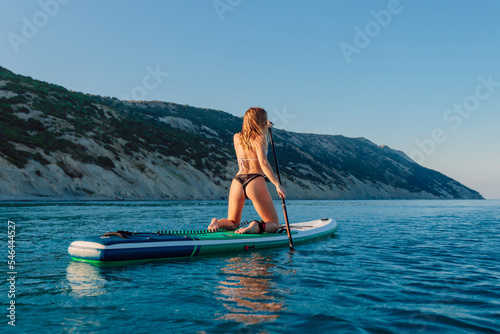 Sporty girl rowing on stand up paddle board at quiet ocean. © artifirsov