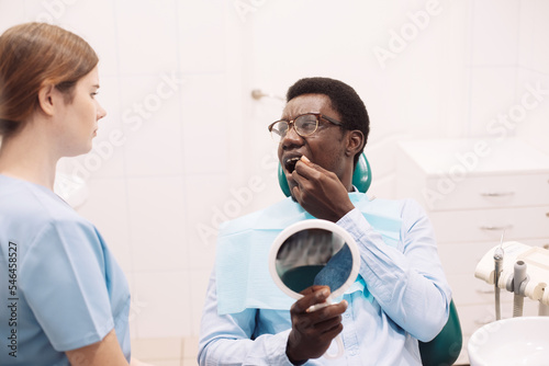 Black male patient showing aching tooth during check up with female dentist Fototapet