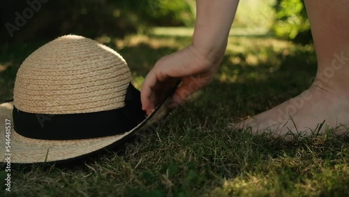 Barefoot female picking up the straw hat from the grass and walk away photo