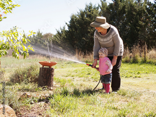 Young two year blonde girl watering plants and gardening with grandmother.