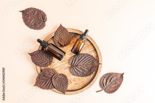 top view of two bottles with an active means to rejuvenate the skin of the face on a wooden round tray with autumn leaves. organic cosmetics.
