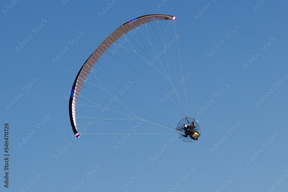 Person riding a paraglider against the blue sky in the background Person riding a paraglider against the blue sky in the background