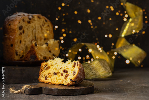 Panettone, Italian Christmas cake with raisins and candied fruits whole and slice on black backgrund with gold ribbon and bokeh. photo
