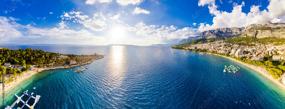 Drone aerial view of Makarska city, Croatia. Sunset over the city, beach and se. Biokovo mountains in the background. Summer time. - obrazy, fototapety, plakaty 