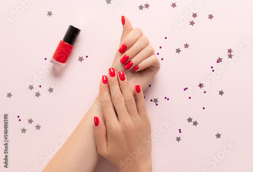 Female hands with trendy red manicure on pink background with confetti. Party, festive, holidays or celebration vibes