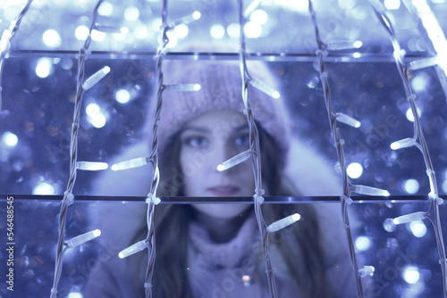 Bright color photo portrait of a beautiful girl in a pink hat with luminous garlands and beautiful bokeh outside in winter